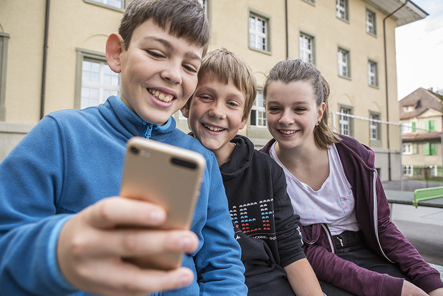Tre bambini che guardano insieme uno smartphone.