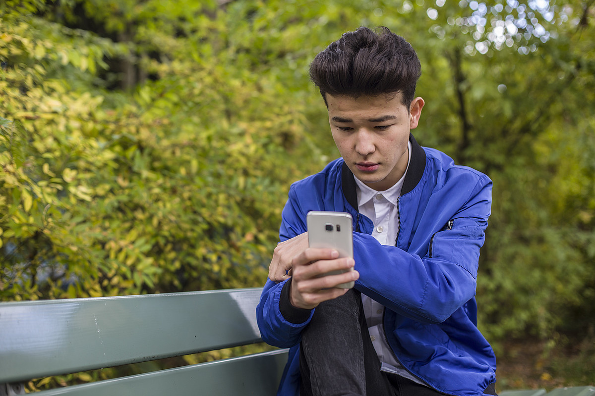 Un ragazzo è fuori ed è al cellulare. Indossa una giacca blu.