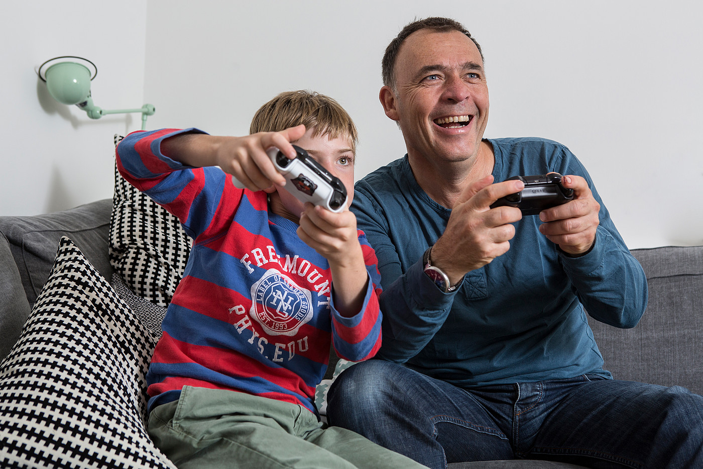 Un padre seduto sul divano con suo figlio che gioca ai videogiochi. 