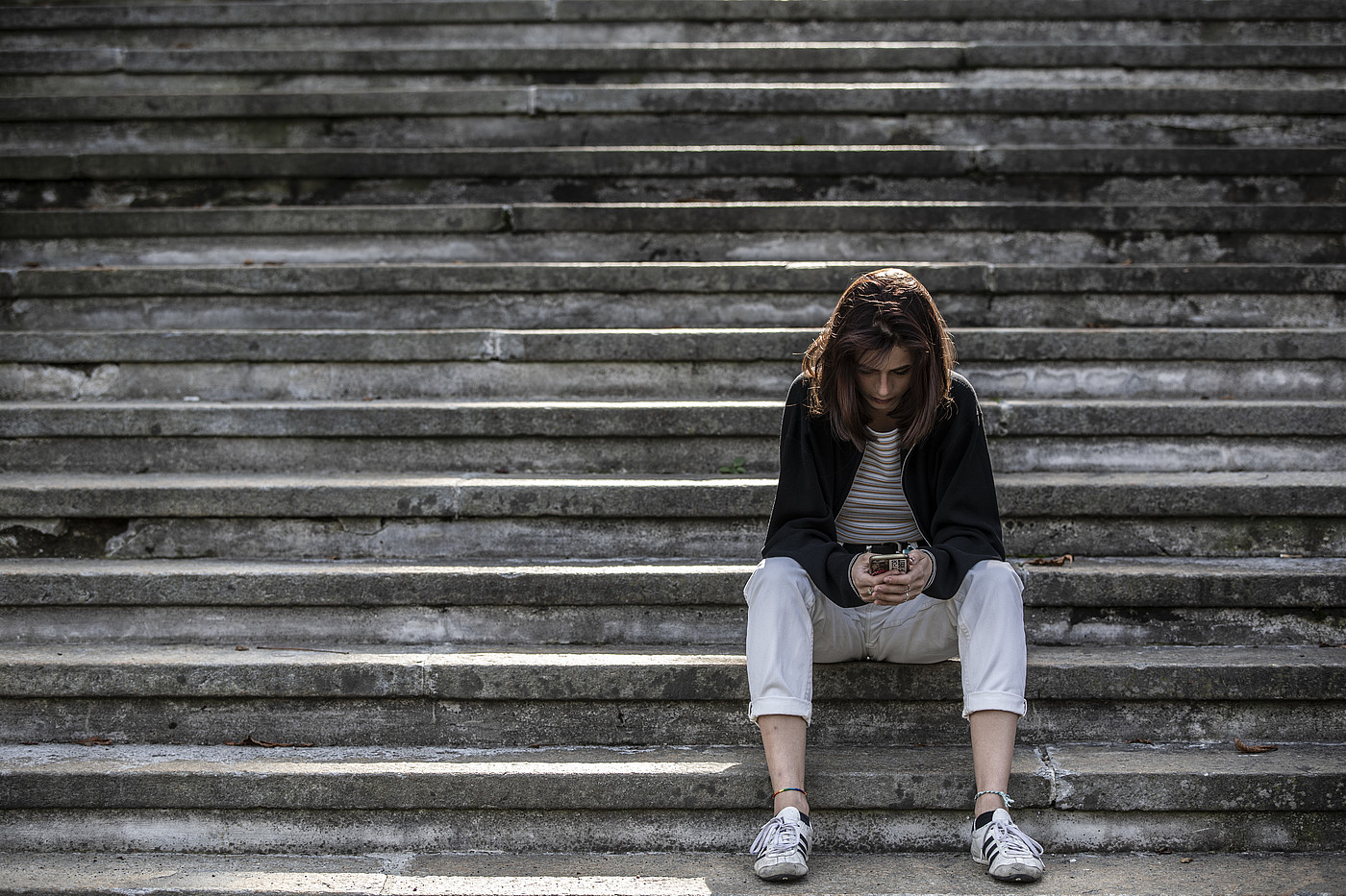 Giovane donna seduta da sola su una scala, che guarda il suo smartphone