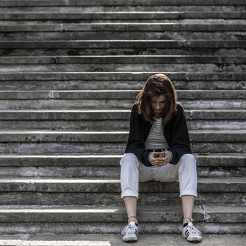 Giovane donna seduta da sola su una scala, che guarda il suo smartphone