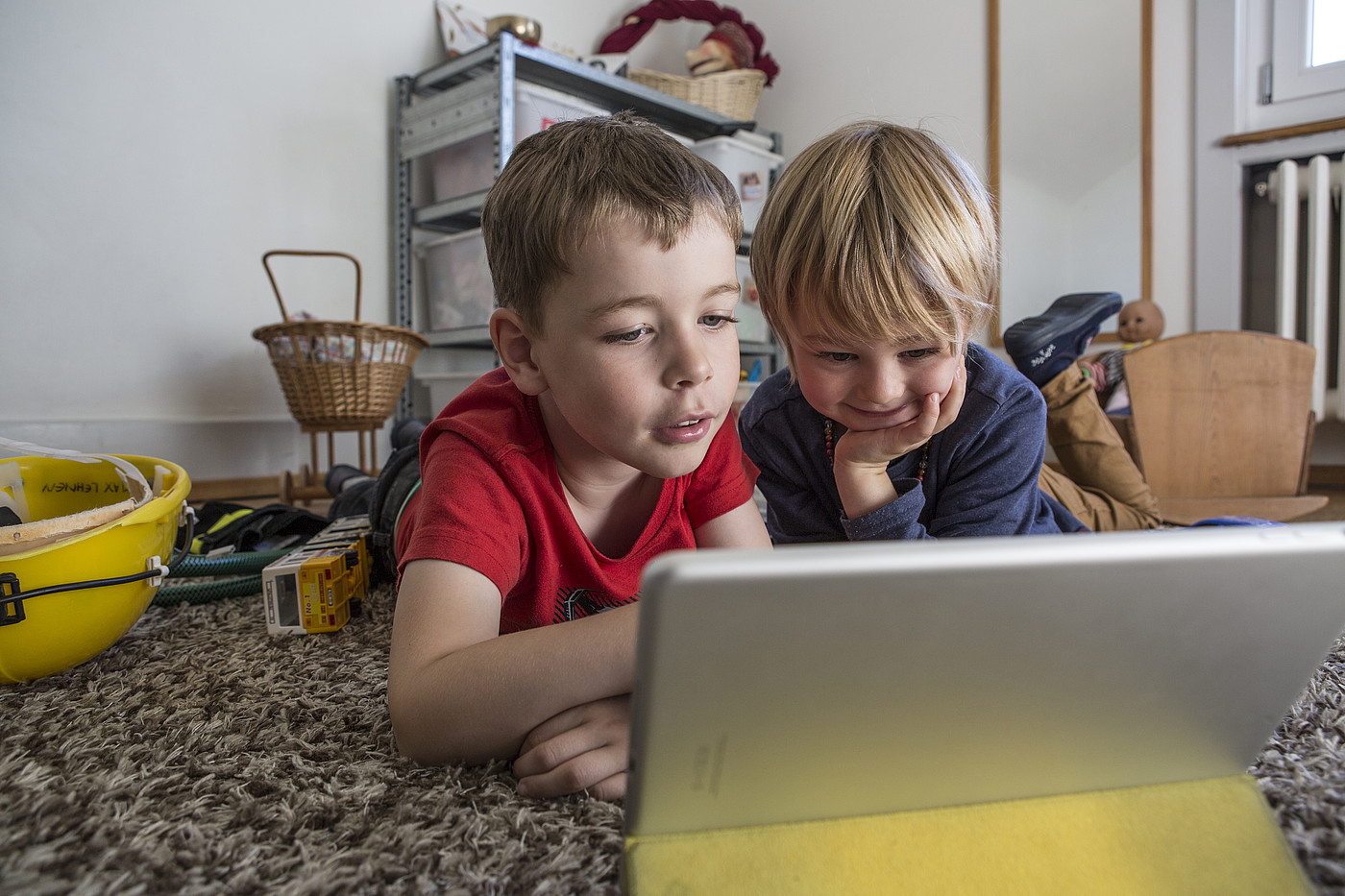 Due bambini sdraiati sul pavimento di un asilo che guardano un tablet.