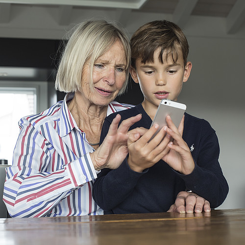 Una donna anziana mostra a un ragazzo come usare uno smartphone.