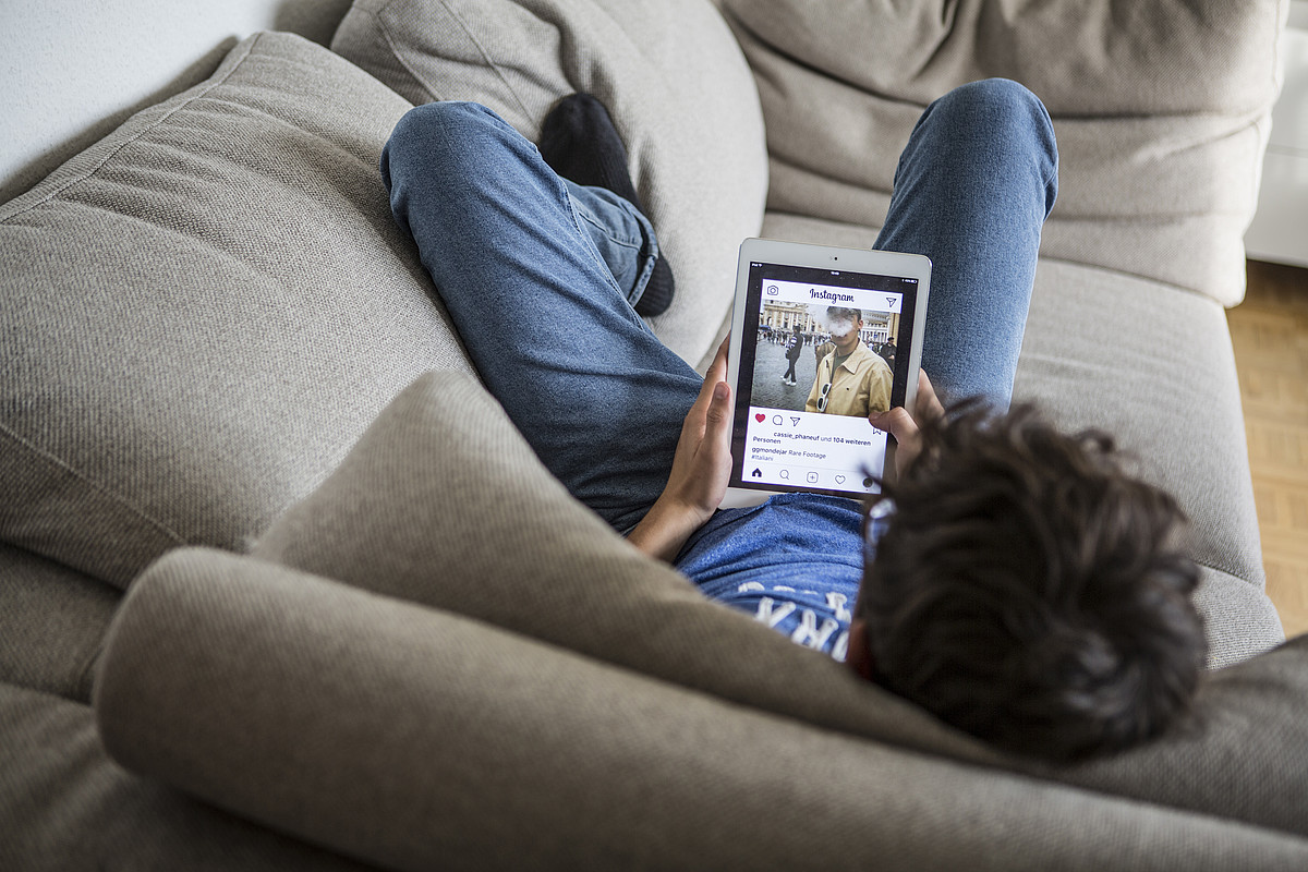 Un adolescente sdraiato sul divano con Instagram aperto sul suo tablet.