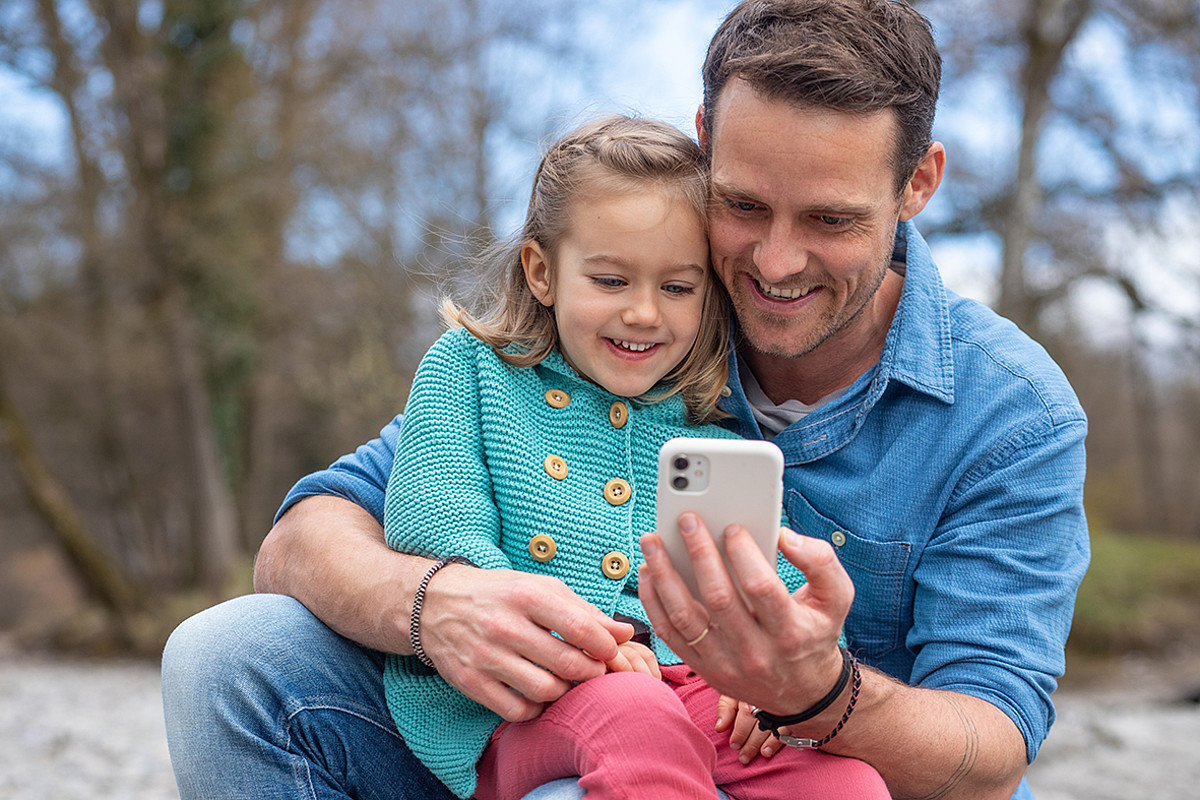 Un padre con un bambino sulle ginocchia che guardano insieme uno smartphone.
