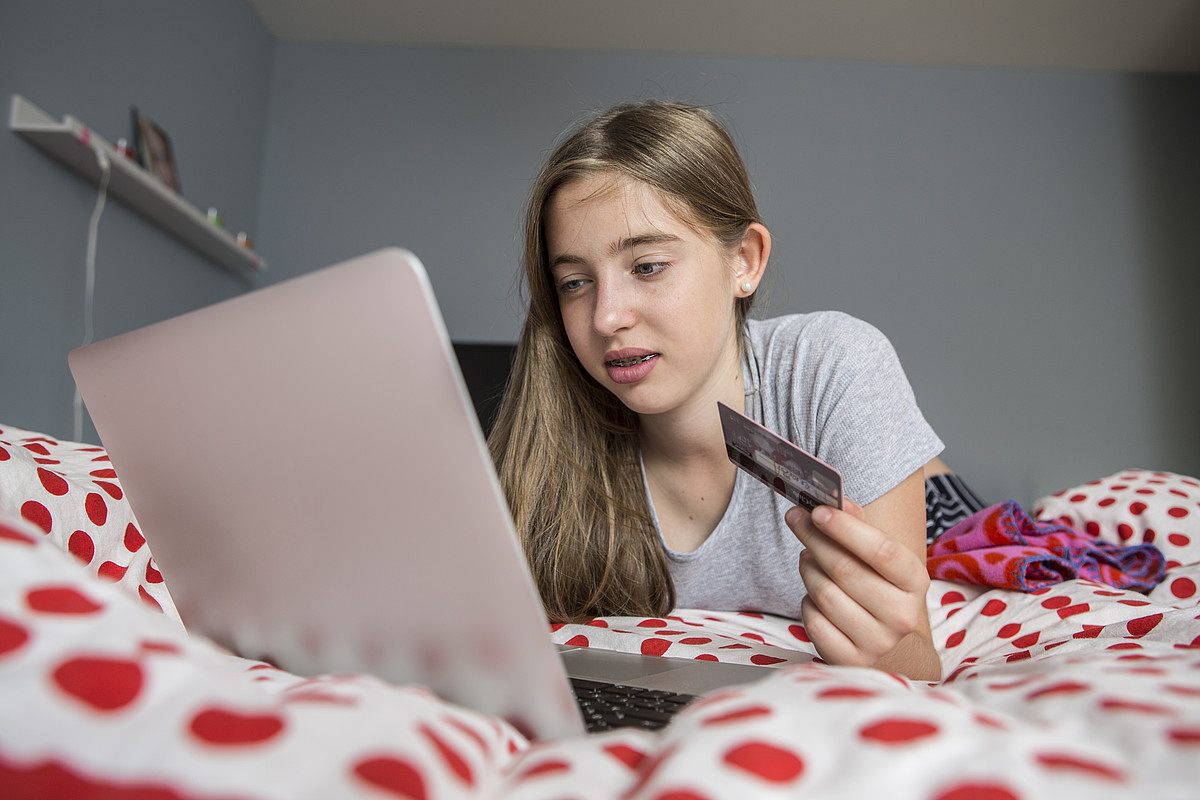 Un'adolescente è sdraiata sul letto con il suo portatile e compra qualcosa con la sua carta di credito.