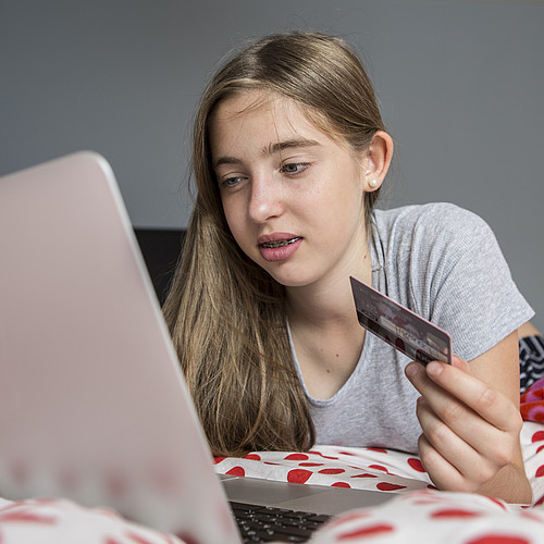 Un'adolescente è sdraiata sul letto con il suo portatile e compra qualcosa con la sua carta di credito.