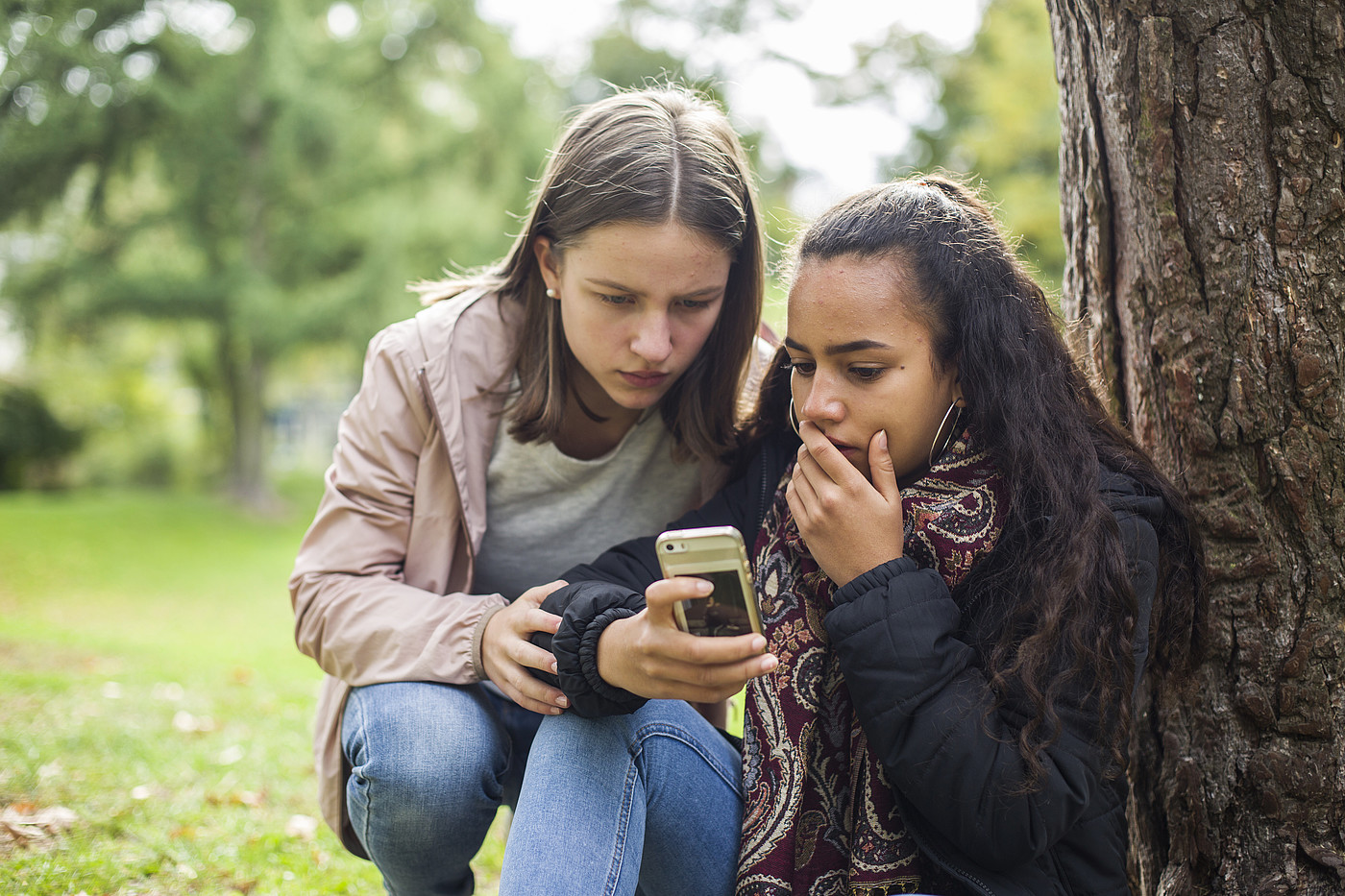 Due adolescenti fuori guardano scioccati un telefono cellulare.