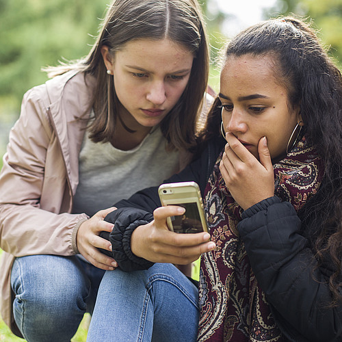 Due adolescenti fuori guardano scioccati un telefono cellulare.