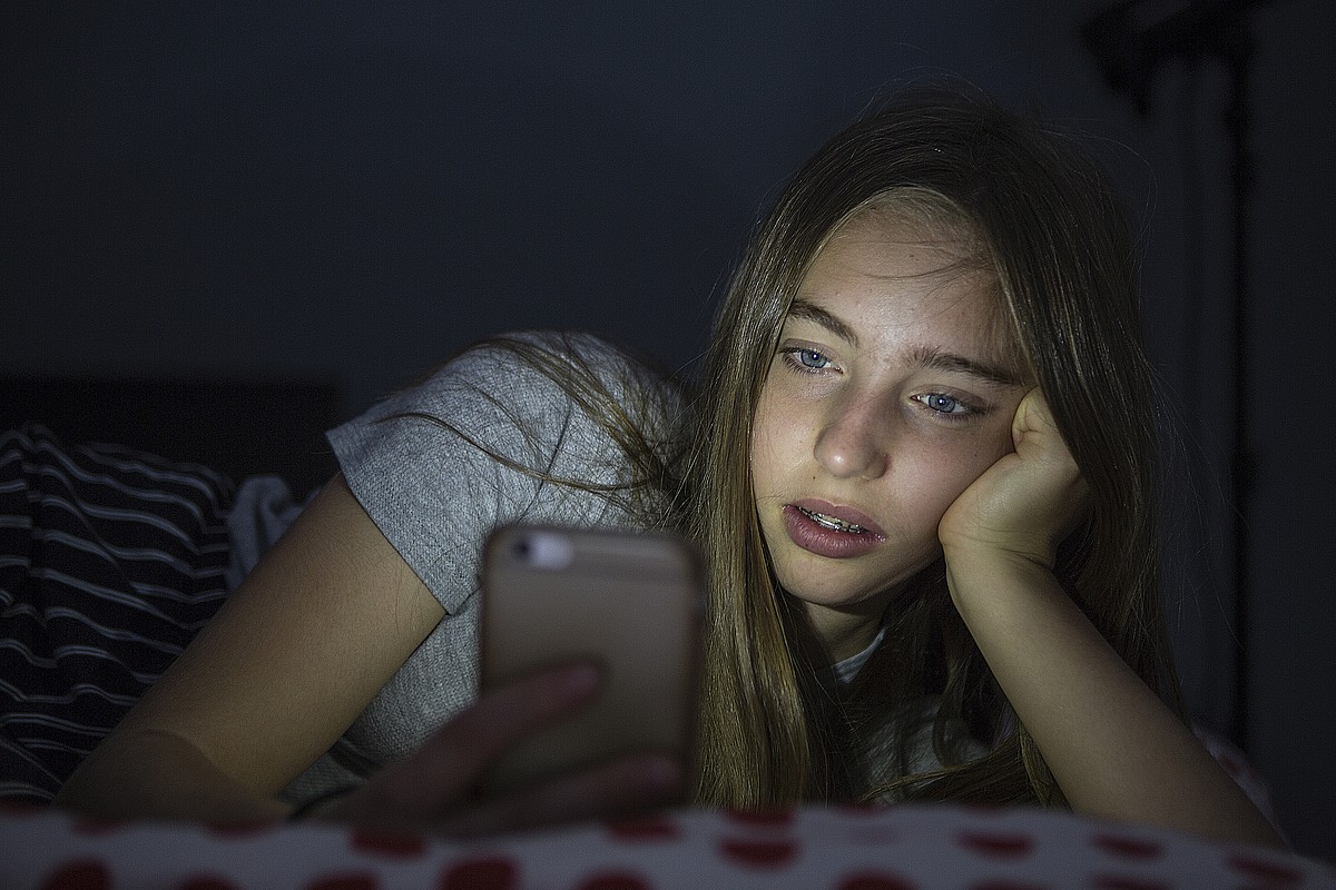 Un'adolescente è sdraiata sul suo cellulare nel buio.