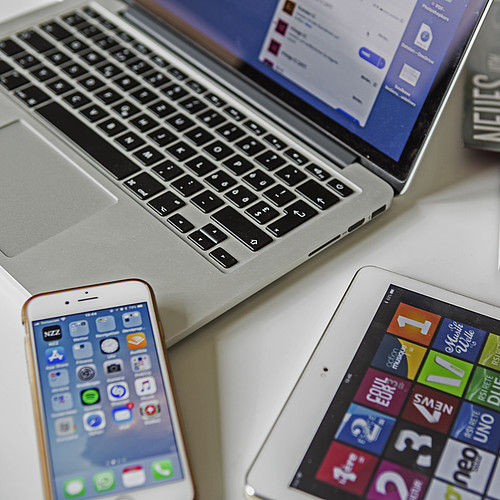 Un computer portatile, uno smartphone, un tablet e delle riviste appoggiate su un tavolo.