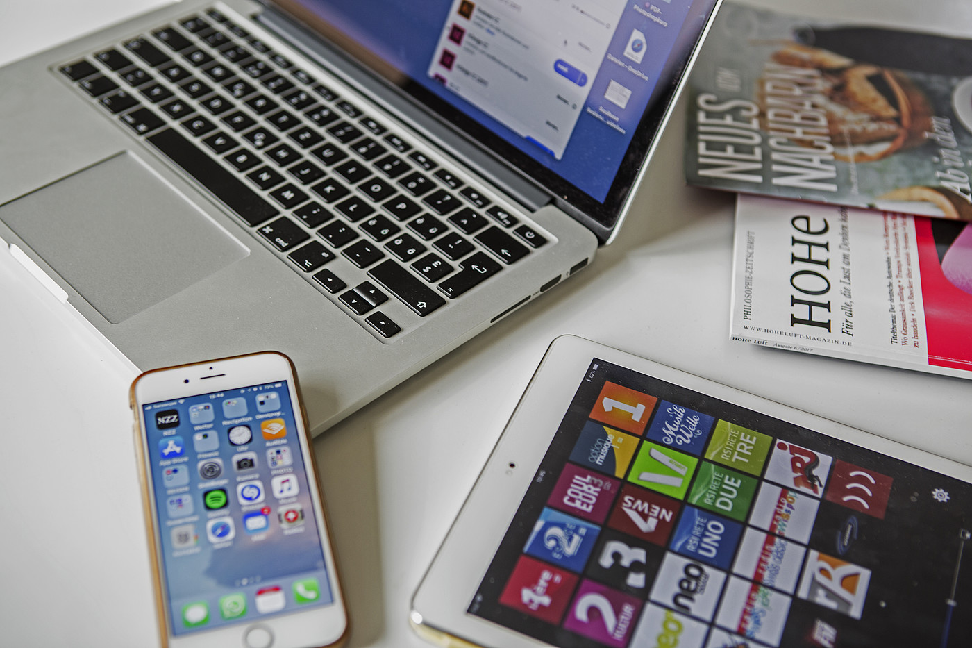 Un computer portatile, uno smartphone, un tablet e delle riviste appoggiate su un tavolo.