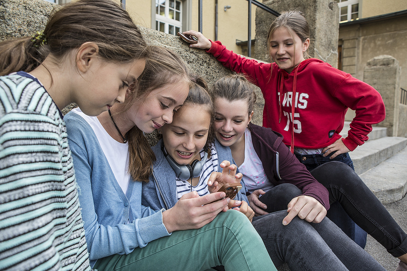 Cinque ragazze adolescenti guardano un telefono cellulare all'esterno. 