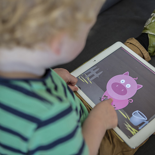 Un bambino sta guardando qualcosa sul tablet. C'è un maiale animato sul tablet.
