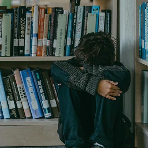 Un ragazzo è seduto rannicchiato sul pavimento della biblioteca. 