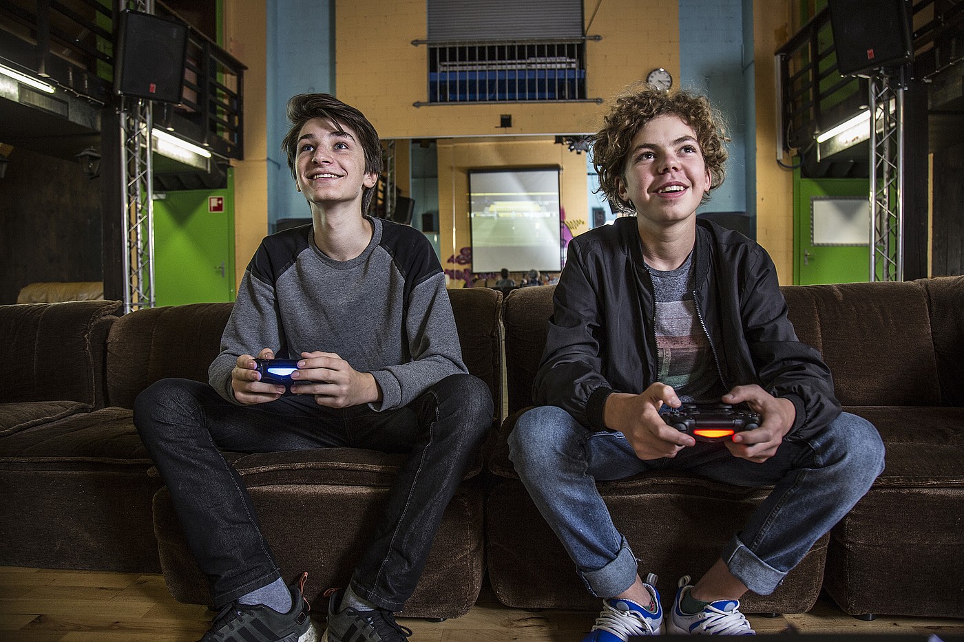 Due adolescenti seduti su un divano in un circolo giovanile che giocano insieme a un videogioco.