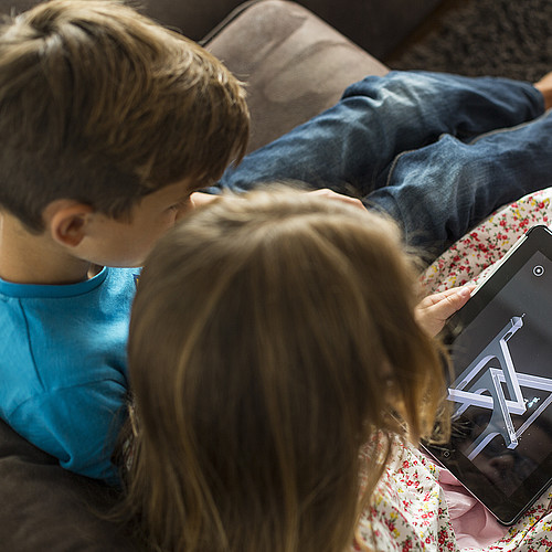 Due bambini seduti su un divano che guardano un tablet.