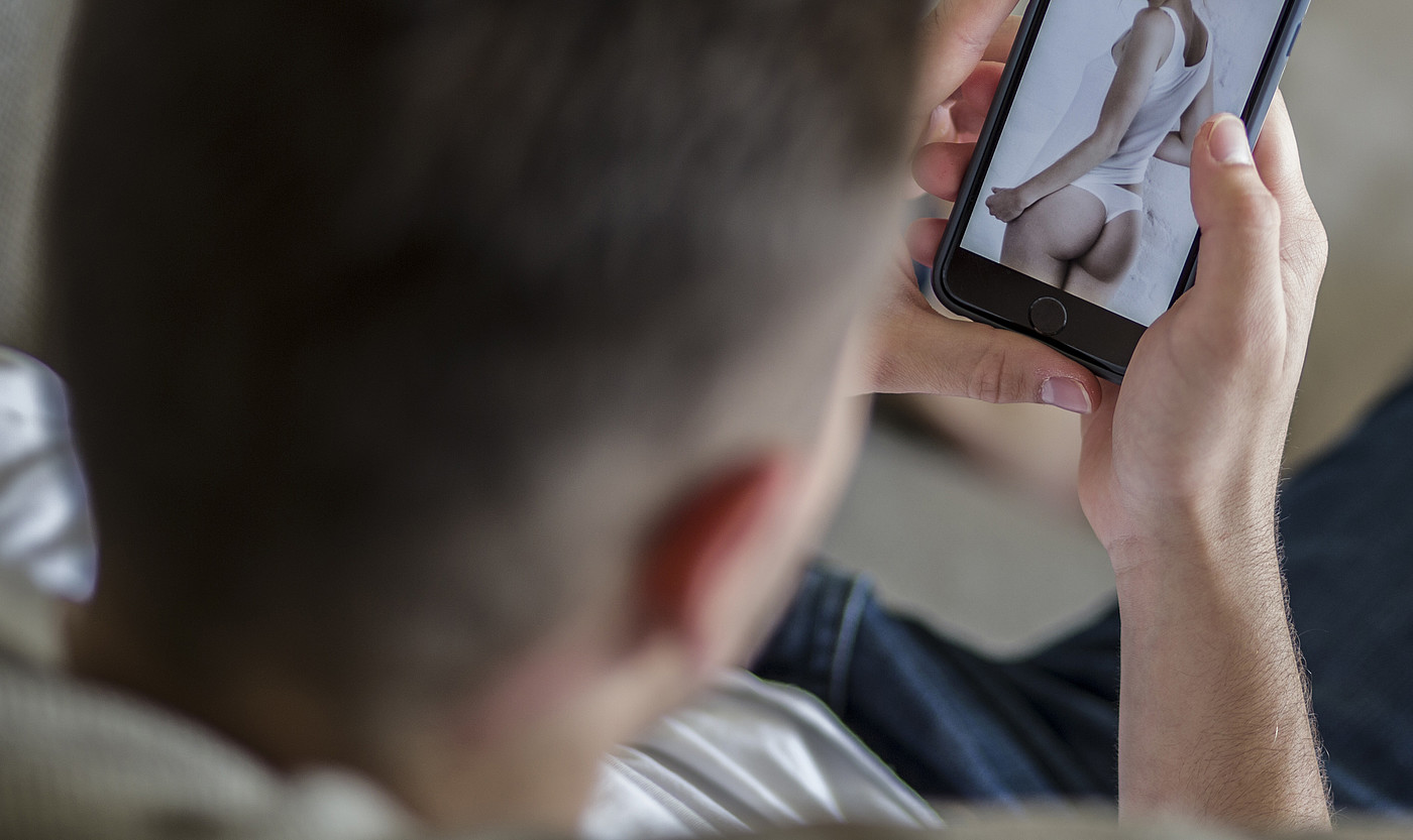 Un giovane uomo guarda la foto di una donna seminuda sul suo cellulare. 